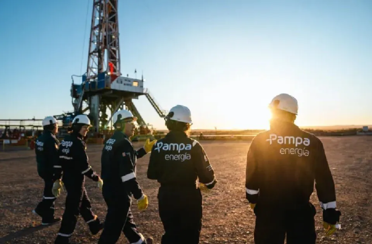 En la imagen, se observa a un grupo de trabajadores de Pampa Energ?a en un sitio de perforación petrolera al amanecer, vestidos con uniformes de seguridad, mientras inspeccionan el ?rea de trabajo en un campo de extracci