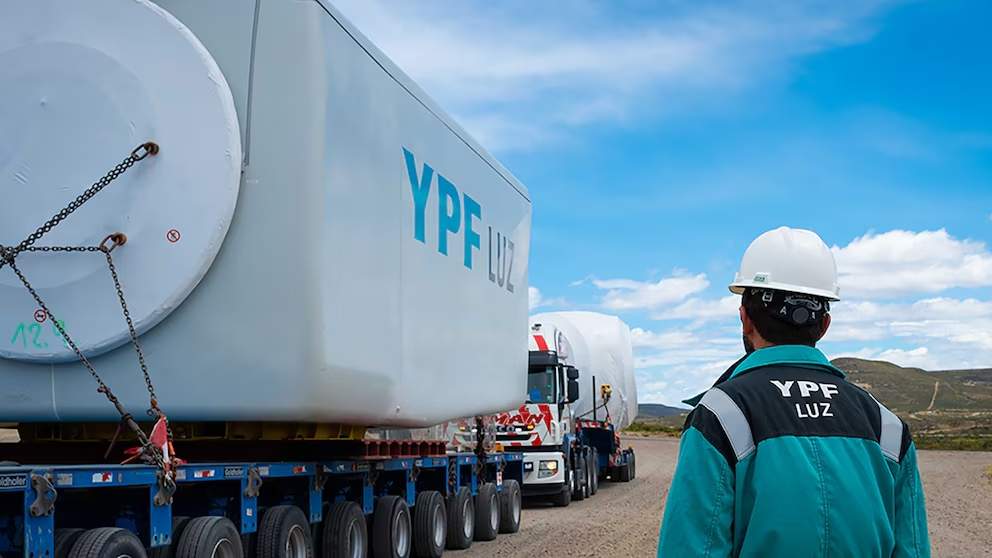 Un operario de YPF manipula una carretilla cargada de sal en una planta de extracción de litio, con montañas y estanques de evaporación visibles en el entorno des?rtico.