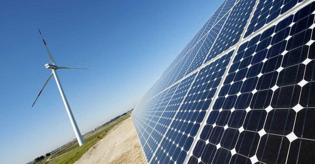 La imagen muestra un parque de energ?a renovable donde conviven paneles solares y una turbina e?lica, ilustrando la integración de energ?a solar y e?lica en un entorno natural para la generación de energ?a limpia.