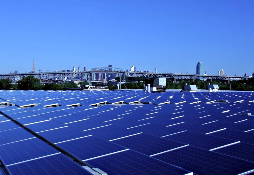 La imagen muestra una granja de paneles solares, con una ciudad en el fondo en el marco de un cielo azul sin nubes.