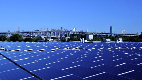 La imagen muestra una granja de paneles solares, con una ciudad en el fondo en el marco de un cielo azul sin nubes.