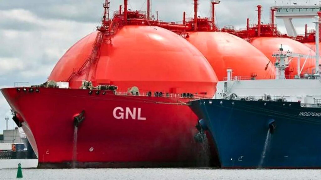 La imagen muestra buques especializados en el transporte de Gas Natural Licuado (GNL), con caracter?sticas distintivas como enormes tanques esféricos de color naranja, dise?ados para mantener el gas en estado l?quido a temperaturas extremadamente bajas. En el casco de uno de los buques se puede leer claramente "GNL". Estas embarcaciones se encuentran en lo que parece ser un puerto o ?rea de carga, con estructuras portuarias visibles al fondo.