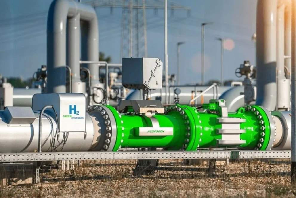 La imagen muestra una tubería industrial de color verde, etiquetada con 'H₂', que transporta hidrógeno. Se aprecian válvulas y sensores en la tubería, lo que sugiere un sistema de control y medición del flujo de hidrógeno.