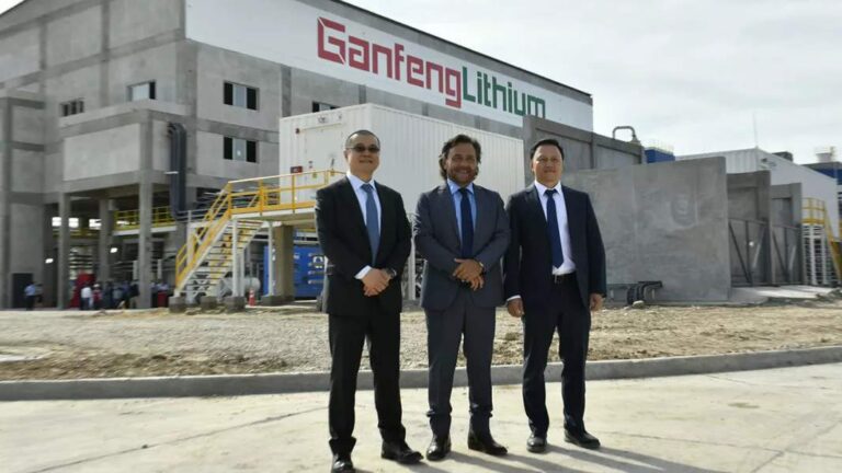 Tres hombres con traje y corbata posan frente a un edificio similar a una f?brica o planta con el logo de Ganfeng Lithium en rojo y verde.
