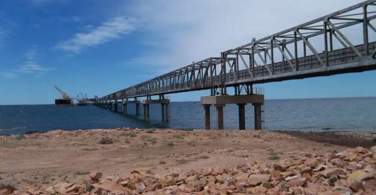 Fotograf?a tomada desde la costa del mar que muestra una instalación energética mar?tima conectada con tierra por un largo puente met?lico.