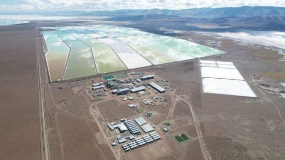 Una instalación de extracción de litio en un paisaje desértico. Se ven grandes estanques de evaporación rectangulares con agua de distintos tonos de verde y blanco. En el centro, una planta industrial con edificios y maquinaria.