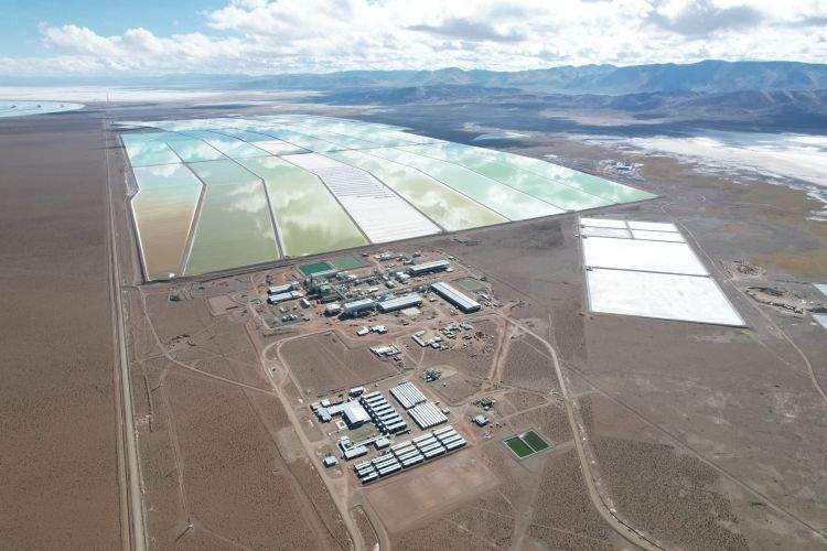 Una instalación de extracción de litio en un paisaje desértico. Se ven grandes estanques de evaporación rectangulares con agua de distintos tonos de verde y blanco. En el centro, una planta industrial con edificios y maquinaria.