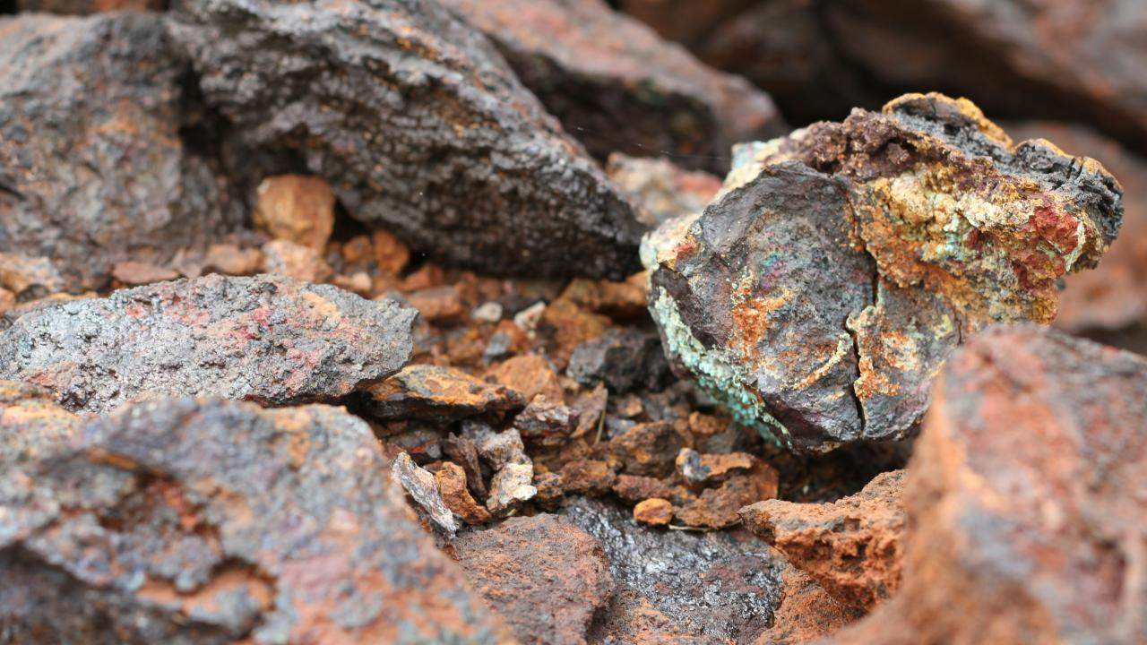 Mineral en bruto con vetas de colores metálicos y óxidos, extraído de una mina a cielo abierto.