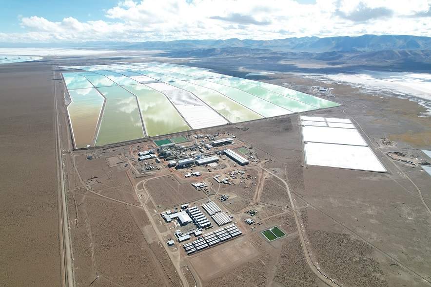 Vista aérea de una planta de extracción de litio en el Salar del Hombre Muerto, Argentina, operada por Ganfeng Lithium. En primer plano se observa el complejo industrial con instalaciones de procesamiento, mientras que al fondo se extienden grandes piletones de evaporación de salmuera, cuyos colores varían según el grado de concentración de litio.