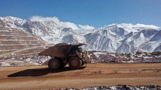Camión minero transportando material en una mina a cielo abierto ubicada en alta montaña, rodeada de cumbres nevadas.
