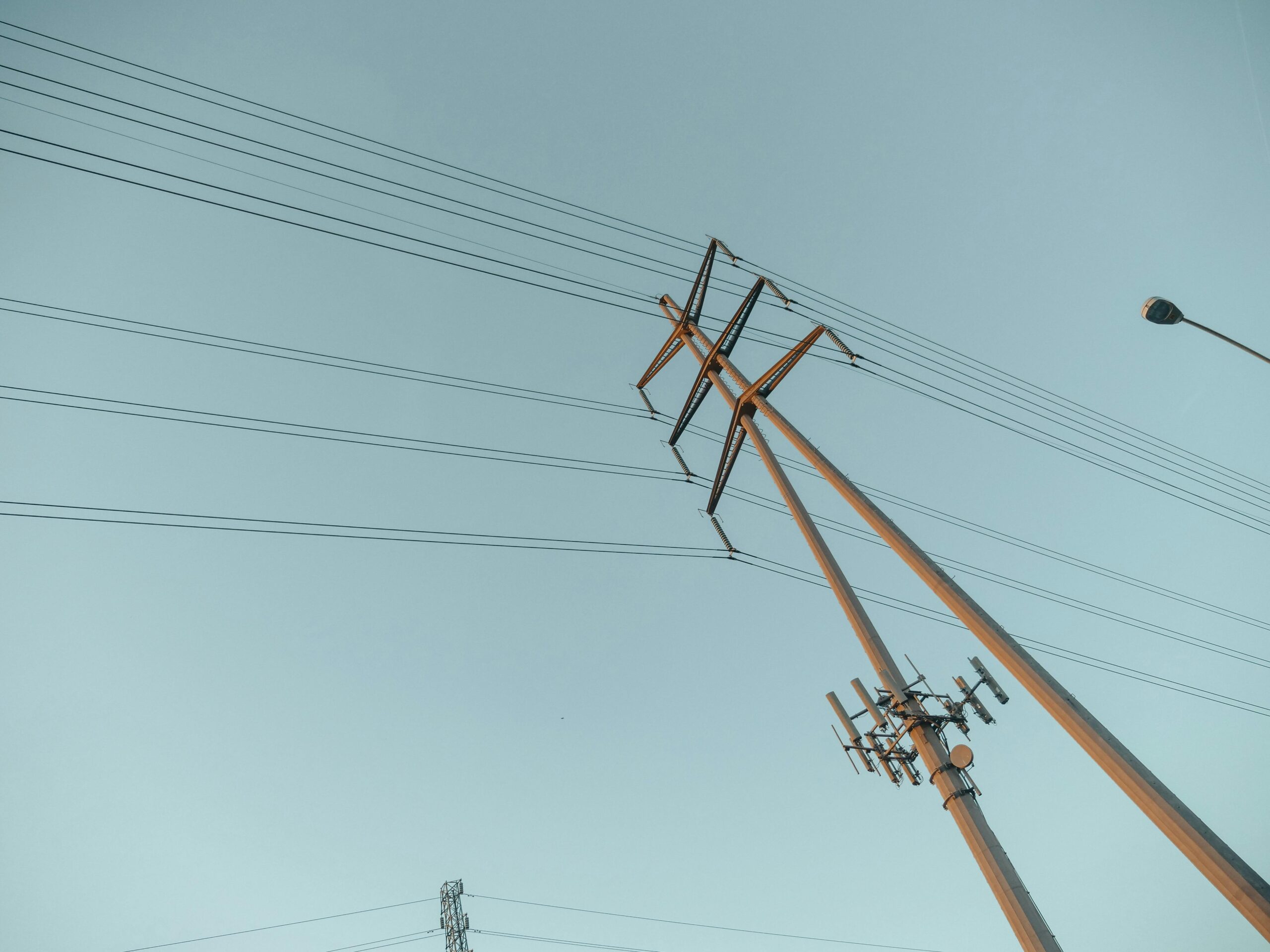 Poste de alta tensión con cables eléctricos y antenas bajo un cielo despejado.