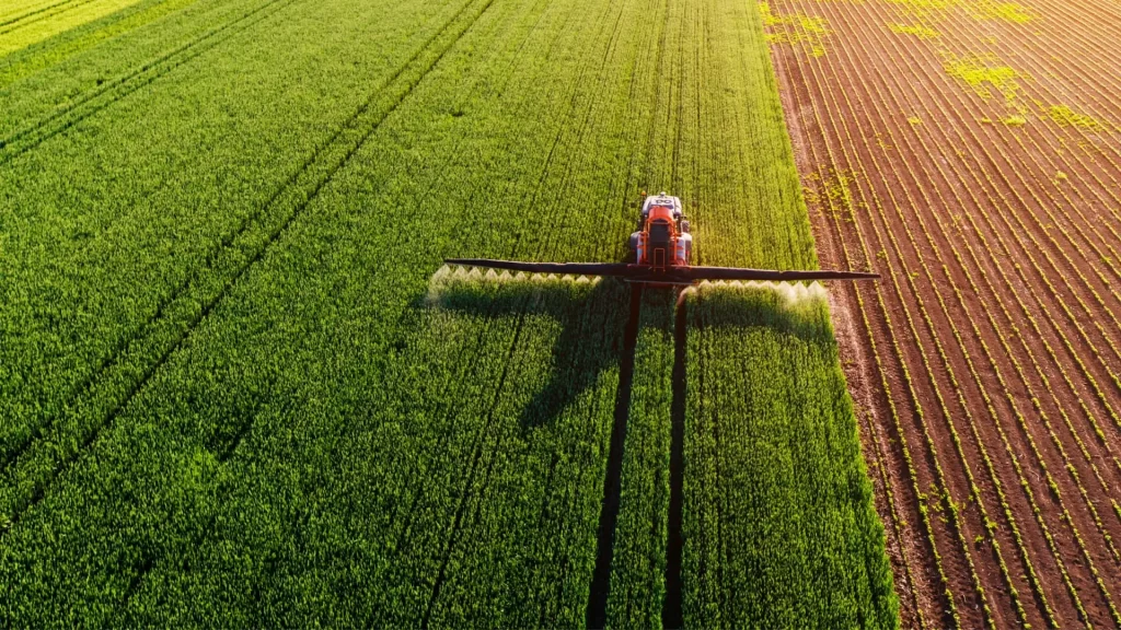 Maquinaria agrícola pulverizando cultivos en un campo visto desde arriba.
