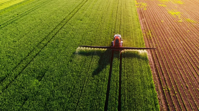 Maquinaria agrícola pulverizando cultivos en un campo visto desde arriba.