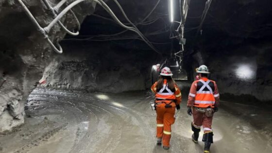 Dos trabajadores con equipo de seguridad recorriendo un túnel subterráneo en una mina.
