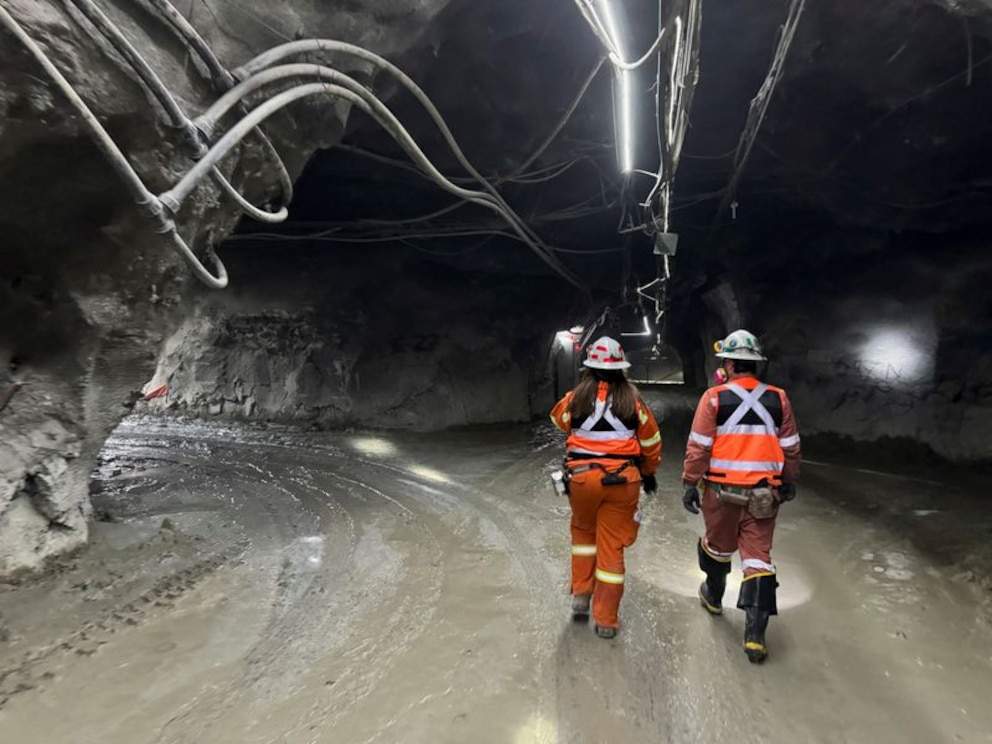 Dos trabajadores con equipo de seguridad recorriendo un túnel subterráneo en una mina.