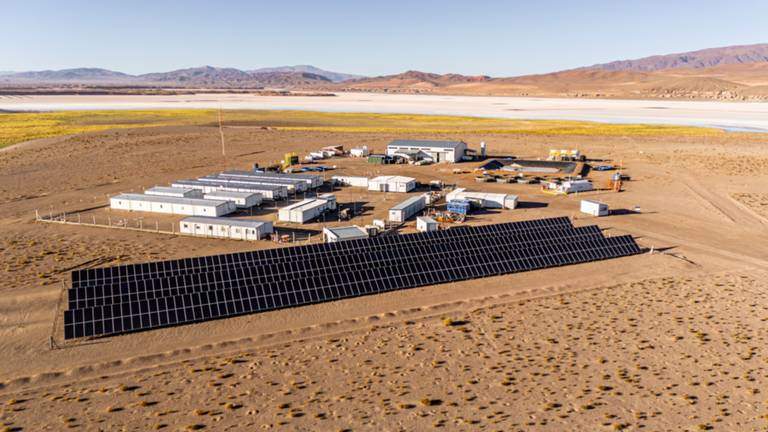 Vista aérea de un campamento minero en el desierto con paneles solares en primer plano y salares al fondo.