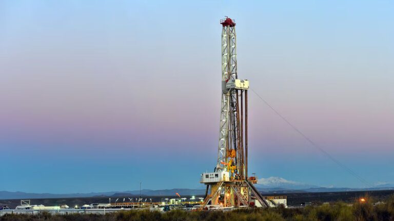 Torre de perforación petrolera en tierra al amanecer, con montañas al fondo.