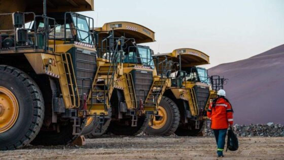 Trabajador de la minería frente a camiones de gran porte en una operación a cielo abierto.