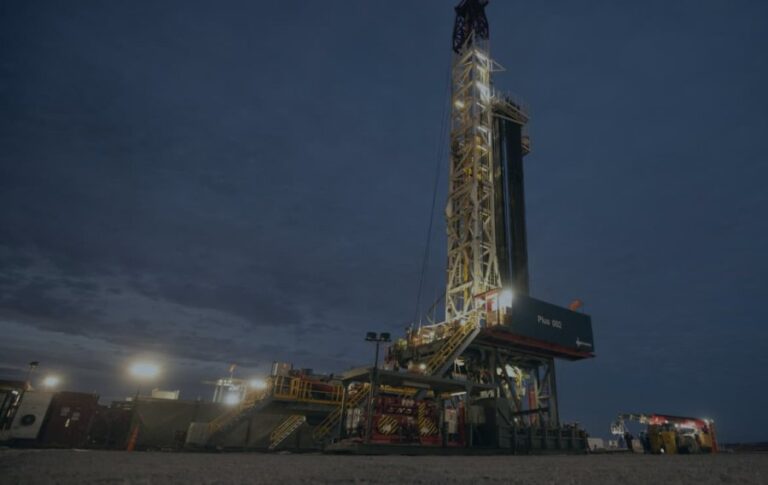 Torre de perforación petrolera iluminada durante la noche en un yacimiento.