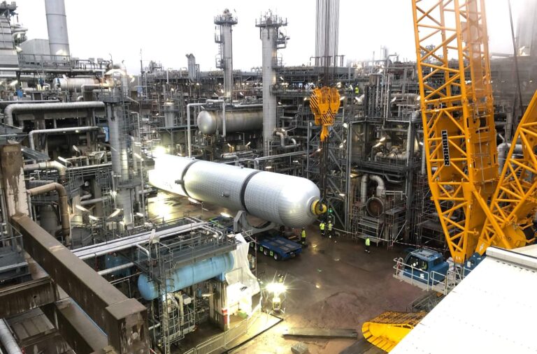 Operación industrial con grúa de gran porte instalando un equipo cilíndrico en una planta petroqu?mica.