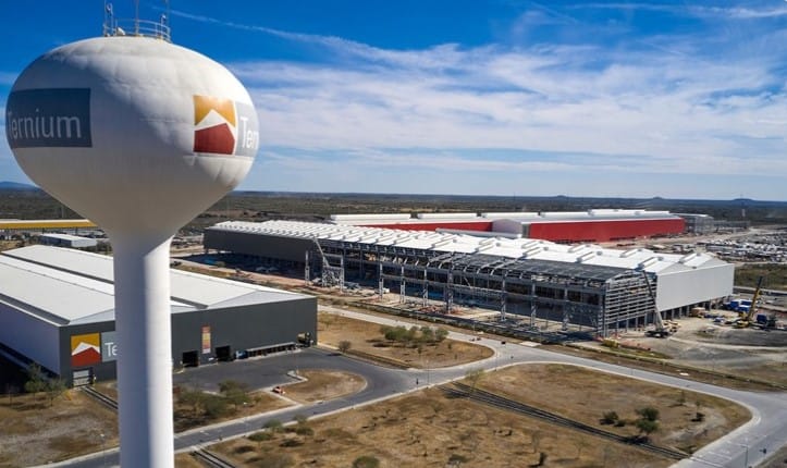 Vista aérea de una planta industrial de Ternium con una torre de agua en primer plano y naves en construcción al fondo.