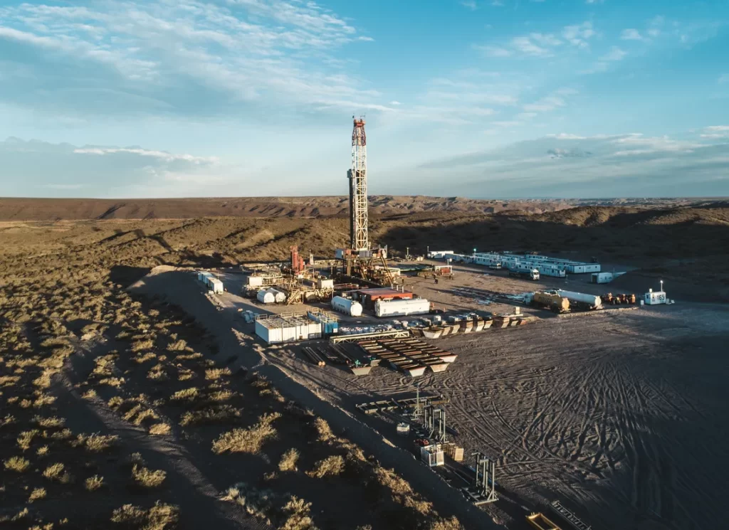 Yacimiento petrolero con una torre de perforación rodeada de instalaciones y equipos en un paisaje ?rido.