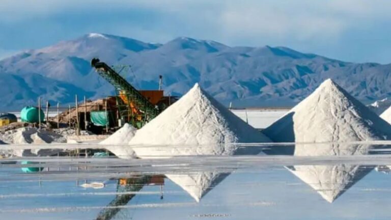 Pilas de sal de litio en salar con instalaciones mineras y montañas al fondo.