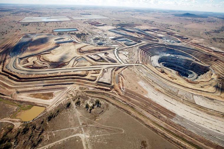 Vista aérea de mina a cielo abierto con instalaciones industriales y caminos escalonados.