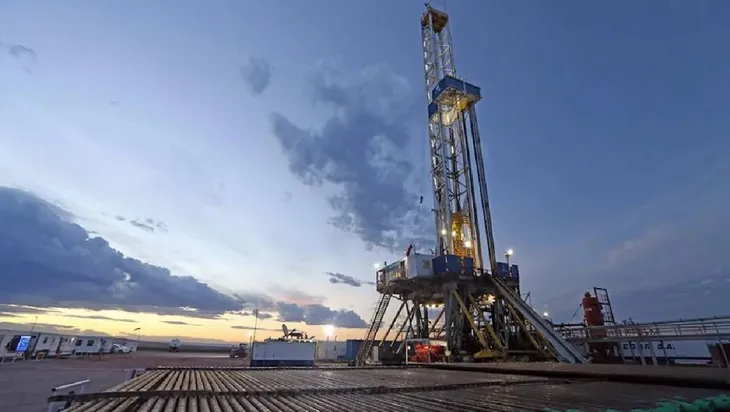 Torre de perforación petrolera iluminada al atardecer en yacimiento terrestre.
