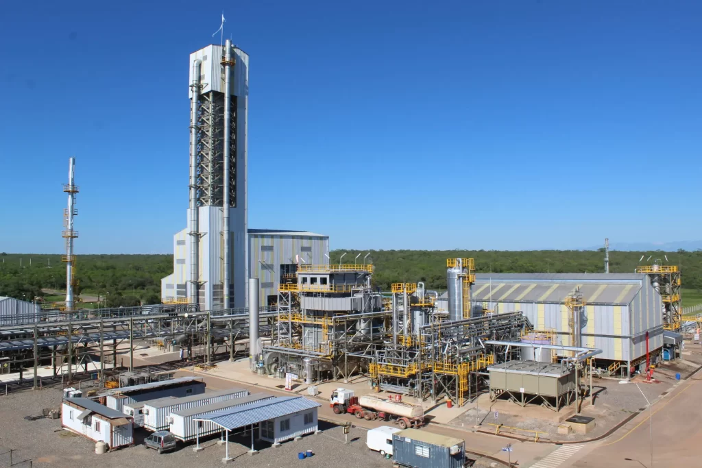 Complejo industrial de gran escala con torres, tuberías y estructuras met?licas, correspondiente a una planta de procesamiento, bajo cielo despejado y rodeada de vegetaci