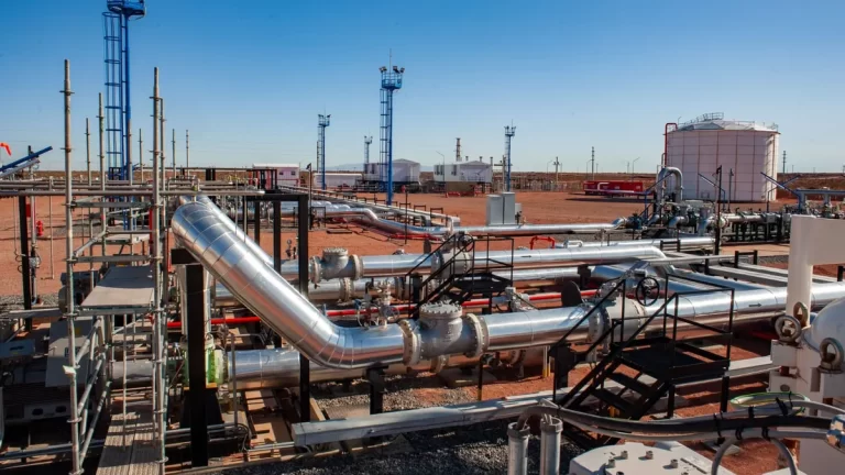 Instalación industrial de transporte de hidrocarburos con oleoductos metálicos, válvulas y torres de control en una planta a cielo abierto, ubicada en una zona árida.