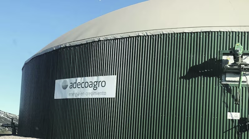 Instalación industrial de biogás con tanque cilíndrico de almacenamiento perteneciente a Adecoagro, bajo cielo despejado.