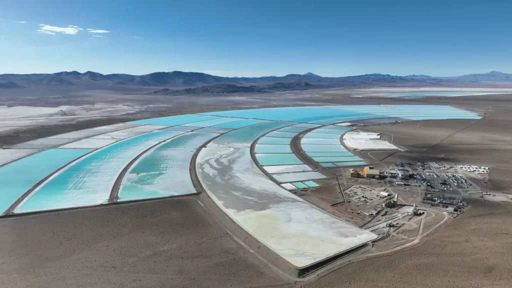 Vista aérea de piletas de evaporación de litio en un salar, con distintas tonalidades de agua y una planta industrial en operación.