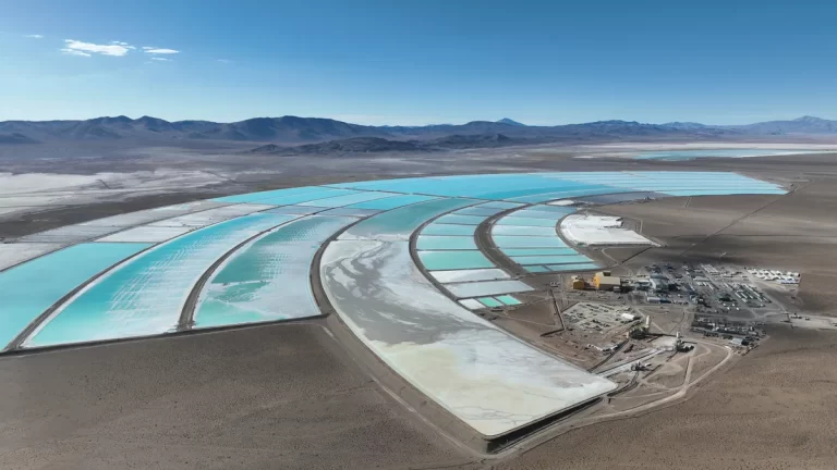 Vista aérea de piletas de evaporación de litio en un salar, con distintas tonalidades de agua y una planta industrial en operación.