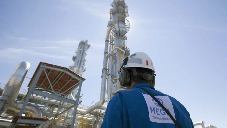 Trabajador con casco y protección auditiva observando estructuras industriales y torres de proceso en una planta energética.
