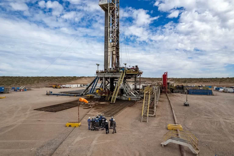 Equipo de perforación petrolera en operación en un yacimiento, con trabajadores reunidos en la base de la torre