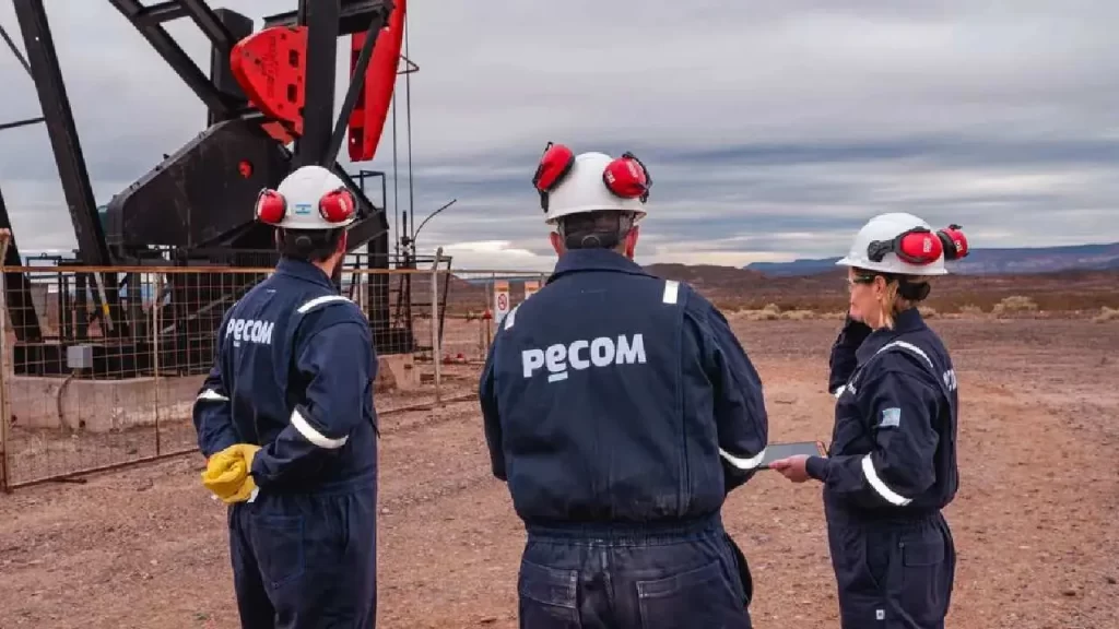 Trabajadores de la empresa PECOM inspeccionan un pozo petrolero con equipo de bombeo en un yacimiento.