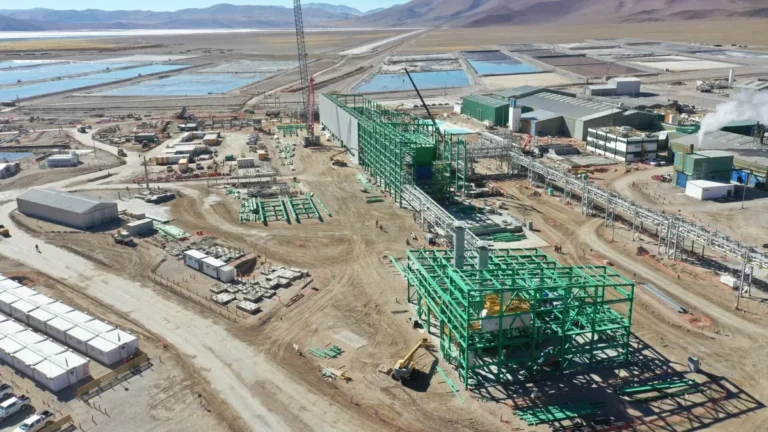 Vista aérea de una planta industrial en construcción en un salar andino, con estructuras metálicas, piletas de evaporación y maquinaria de obra.