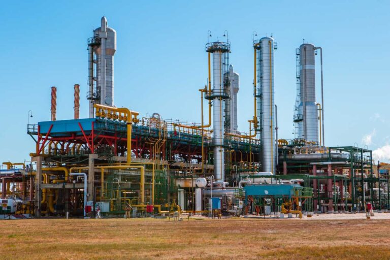 Planta industrial de procesamiento de gas e hidrocarburos, con torres de destilación, tuberías y equipos de procesamiento en un complejo energético al aire libre.