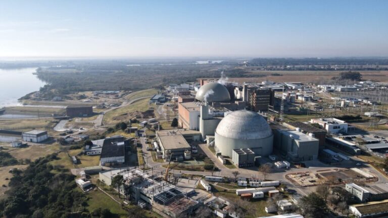 Vista aérea de una central nuclear junto a un río, con edificios de contención e infraestructura industrial.