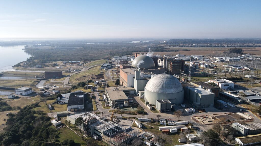Vista aérea de una central nuclear junto a un río, con edificios de contención e infraestructura industrial.
