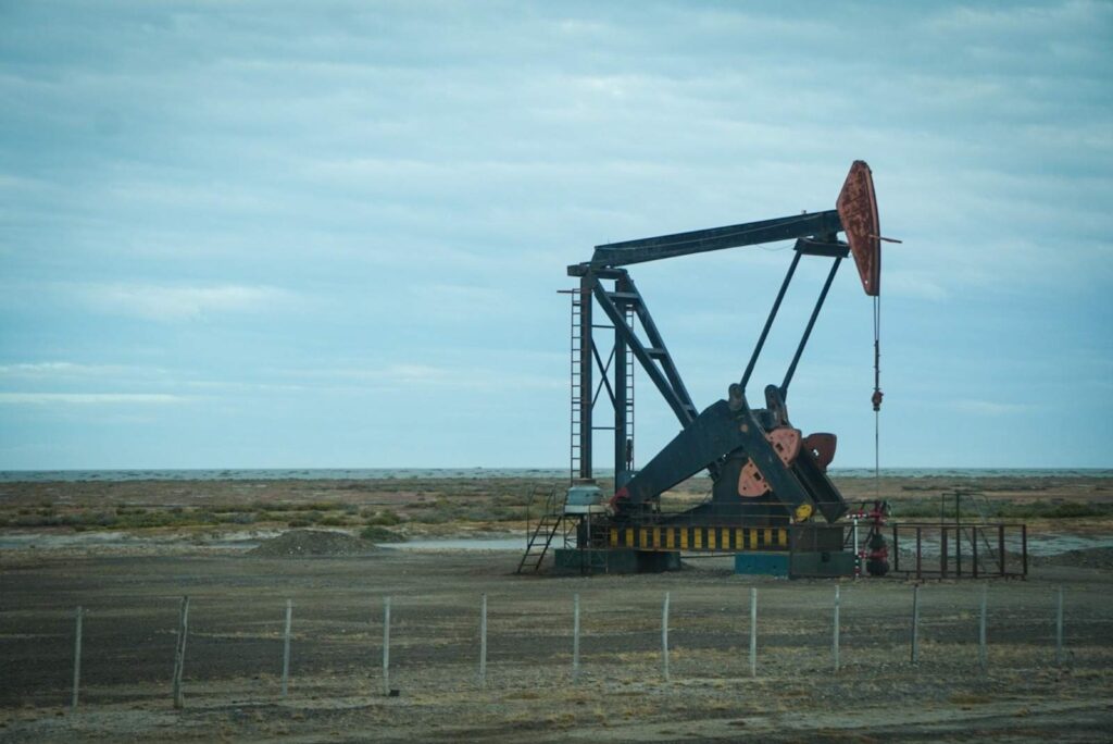 Bomba de extracción de petróleo operando en un yacimiento terrestre, rodeada por un paisaje árido y cercado bajo un cielo nublado.