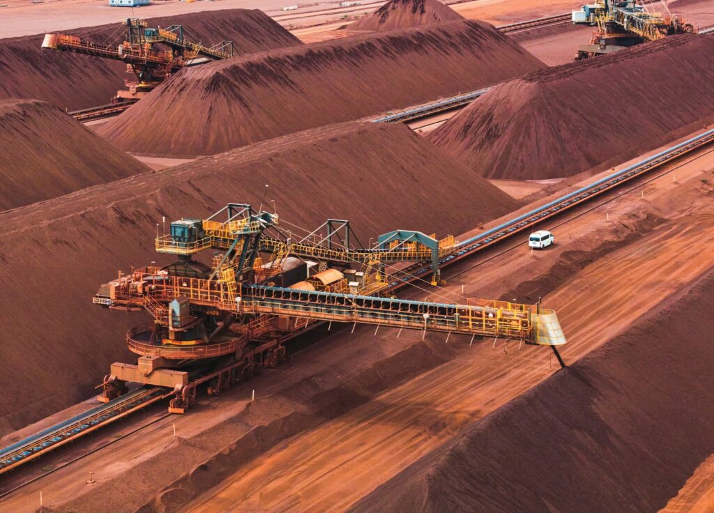 Maquinaria industrial y cintas transportadoras operando entre montículos de mineral en un centro de acopio minero.