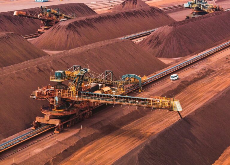 Maquinaria industrial y cintas transportadoras operando entre montículos de mineral en un centro de acopio minero.