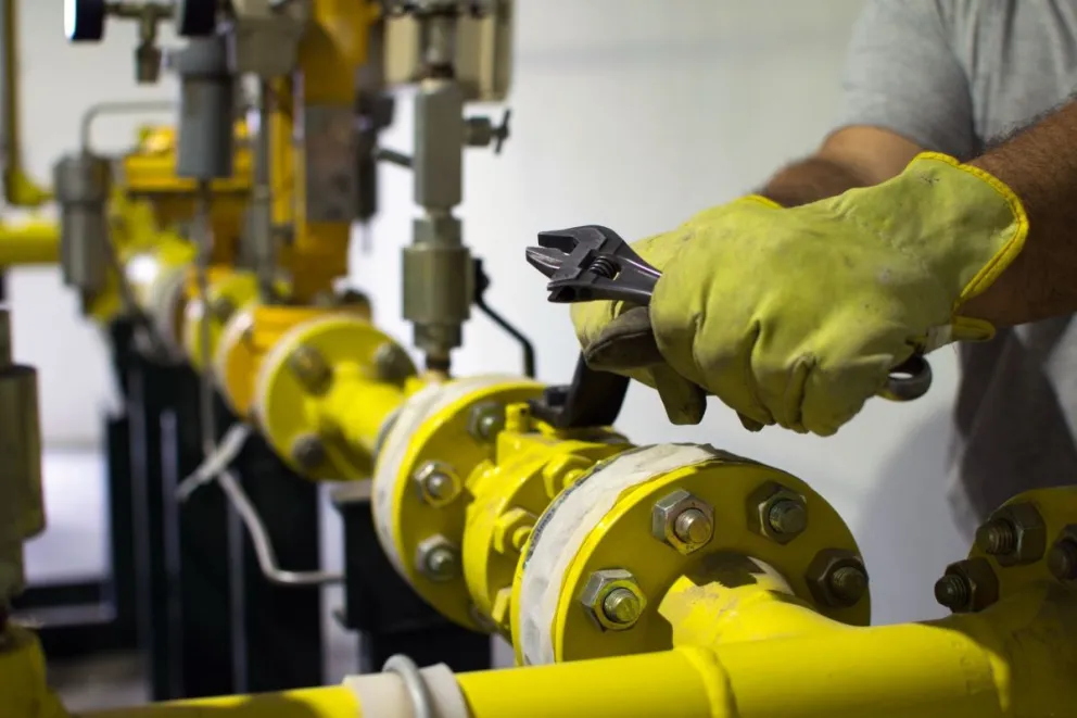 Primer plano de un operario utilizando una llave para realizar tareas de mantenimiento en válvulas y tuberías de una instalación de transporte de gas.